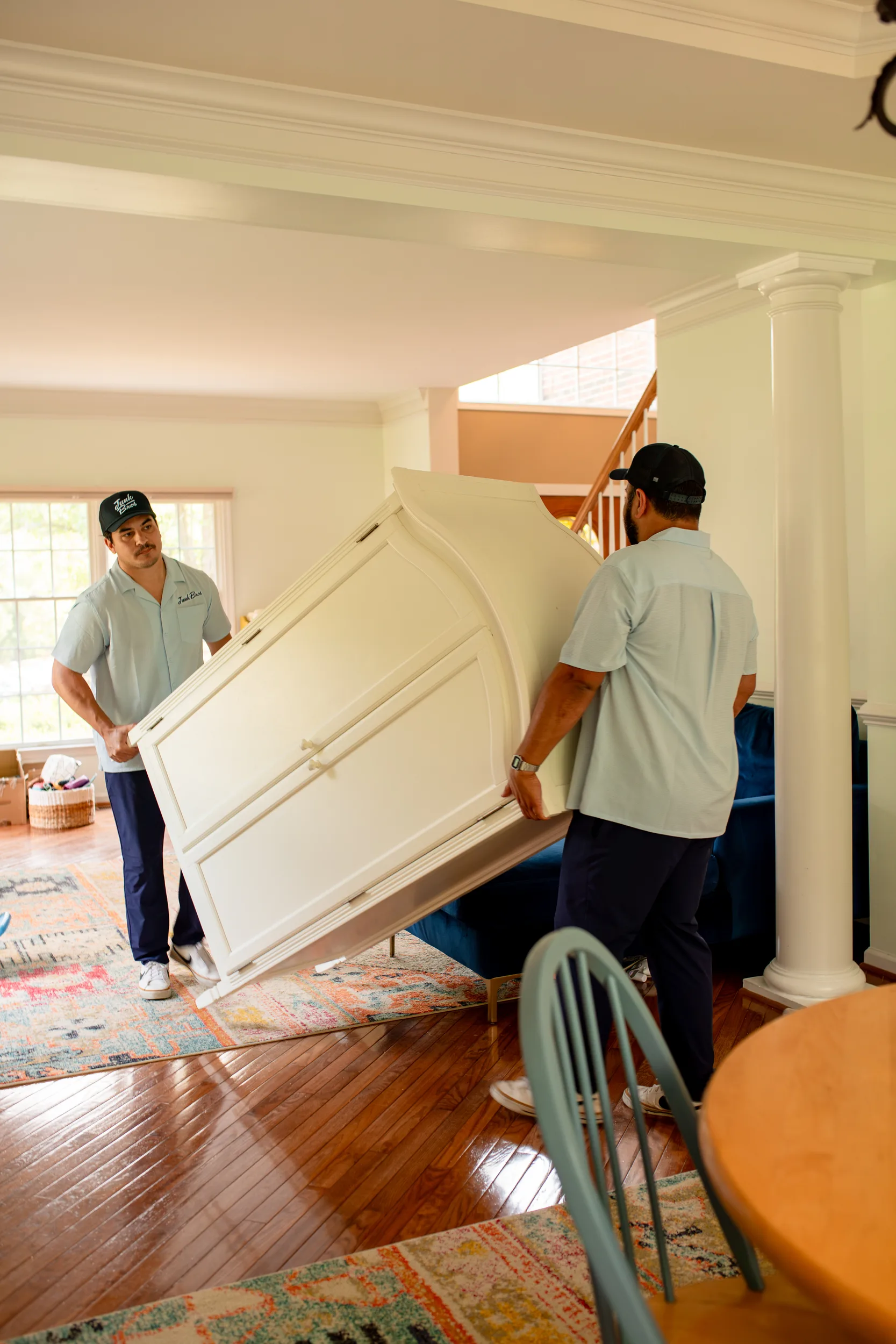 Two Junk Bros crew members carrying an armoire out through the house
